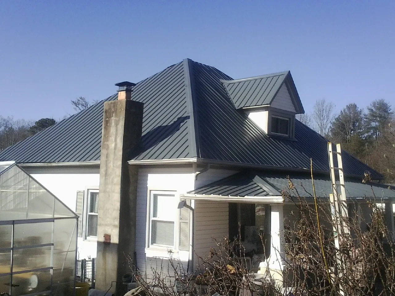 Dark blue standing seam metal roof on a white farmhouse with dormer — Slate & Tile Roof Repair by Roofing Brothers in Zenda