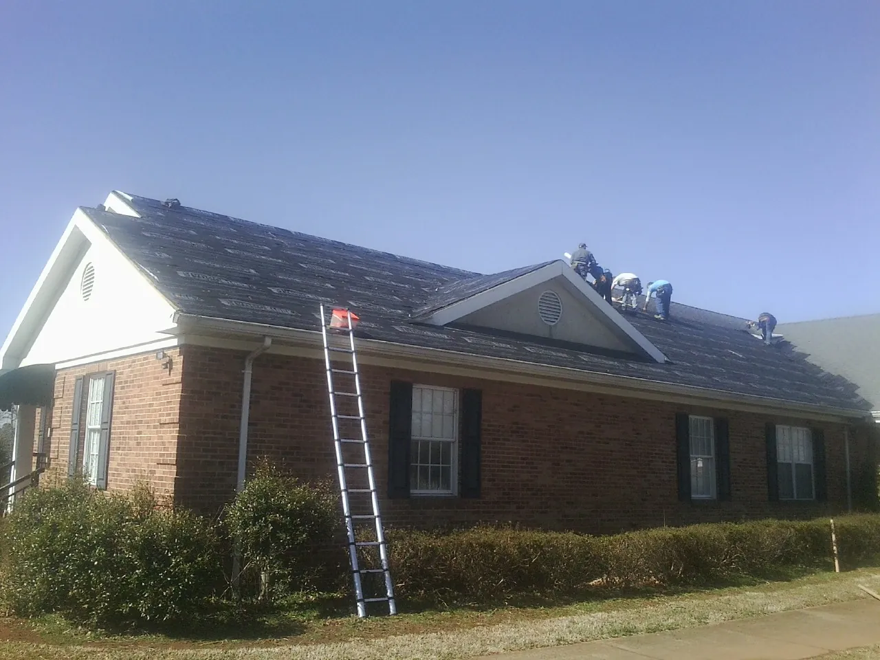 Crew tearing shingles off a brick ranch roof with a ladder set — Metal Roof Repair work by our crew in Zenda