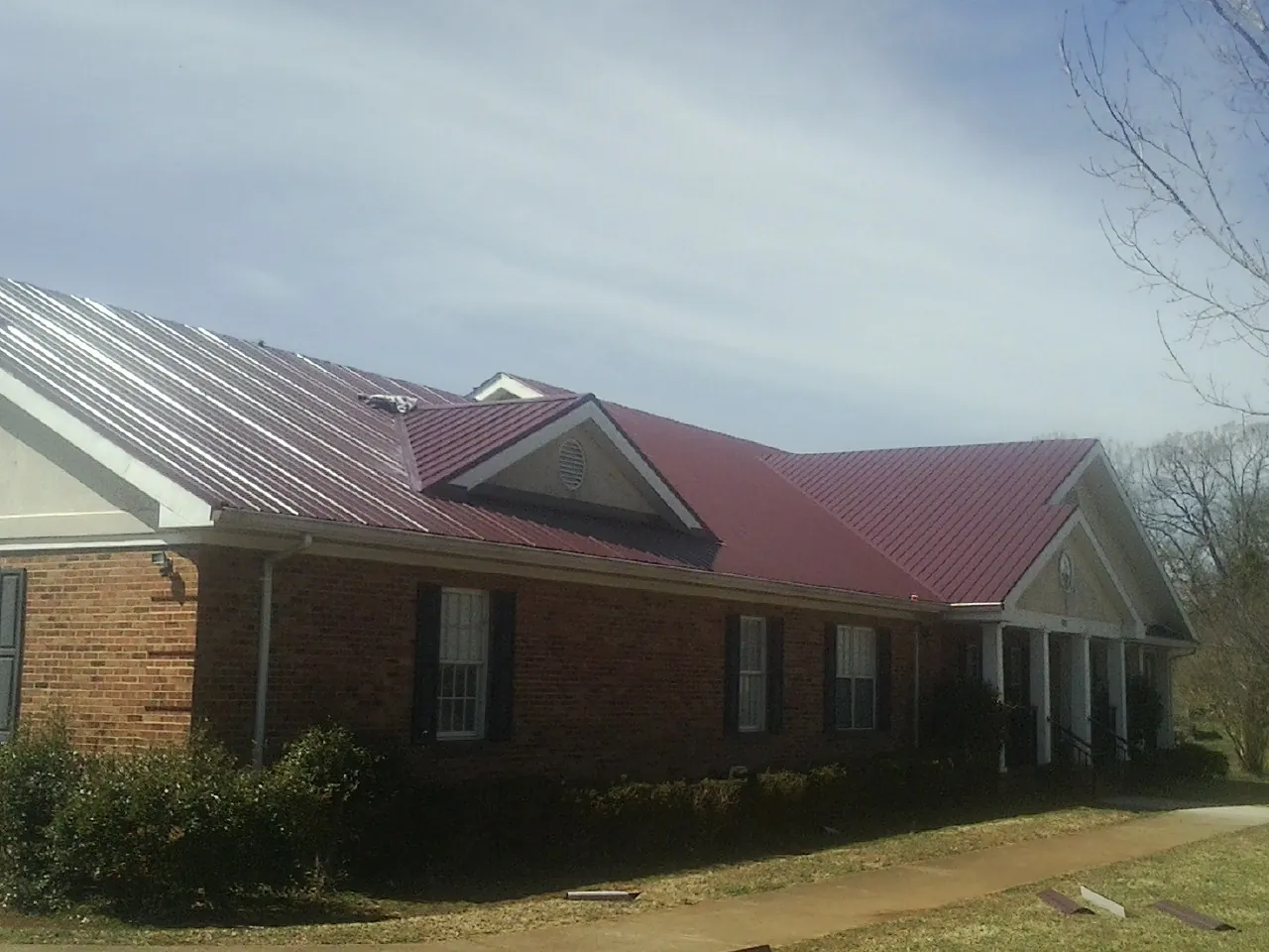 Red metal roof with gabled entries on a long brick building, from a Hail Damage Roof Repair job in Zenda