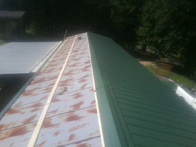 Old rusted panels beside newly installed green metal roofing — Wind Damage Roof Repair by Roofing Brothers in Zenda