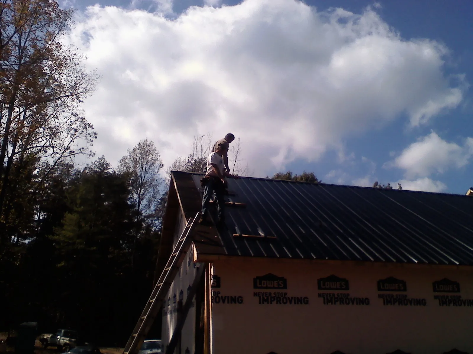 Roofer fastening dark metal panels high against a cloudy sky, from a Roof Inspection job in Zenda