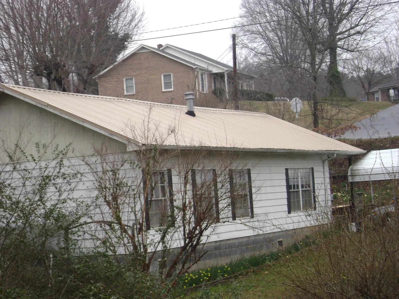 Tan metal roof on a white sided house set into a hillside — Commercial Roofing by Roofing Brothers in Zenda